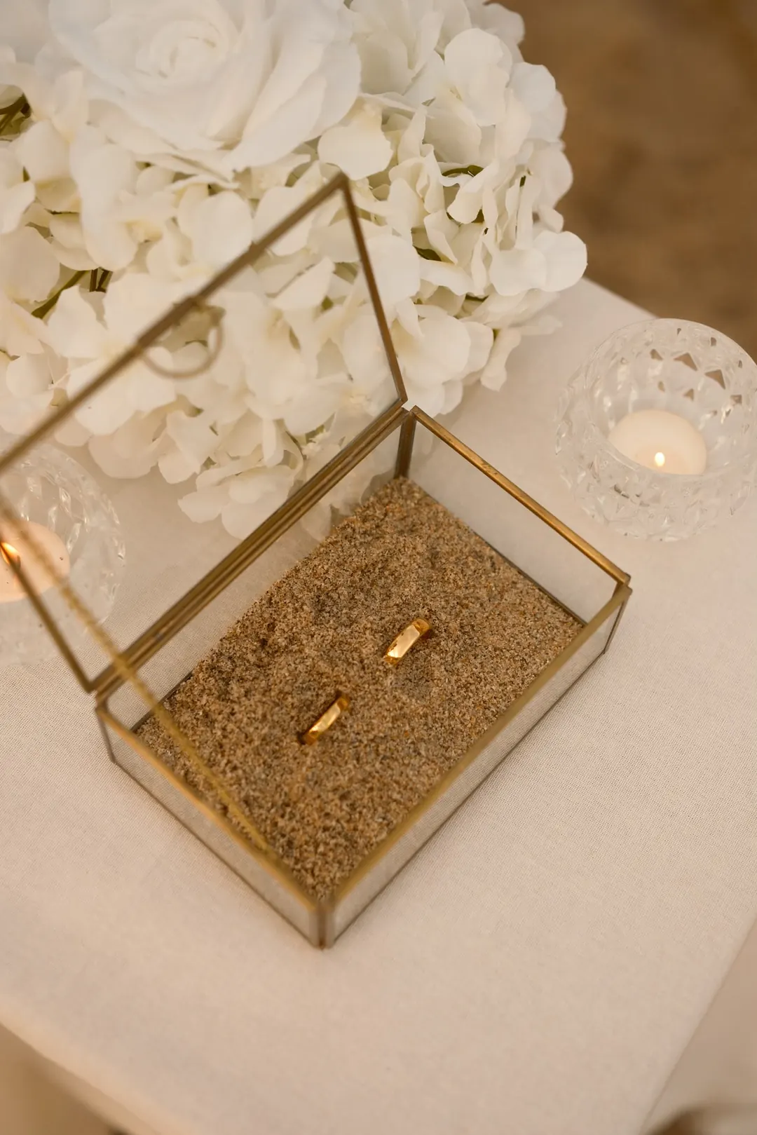 The wedding rings resting in a glass box filled with sand