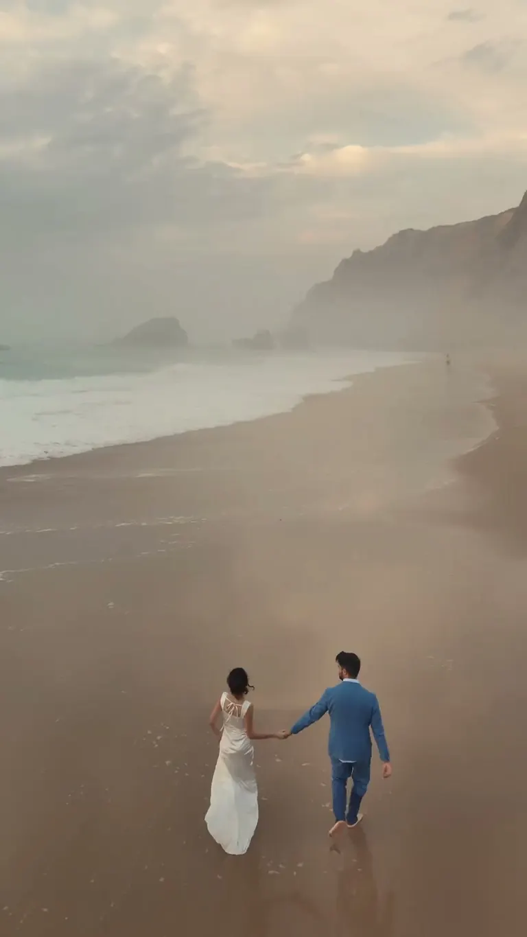From above, the newlyweds walk hand in hand along the shore