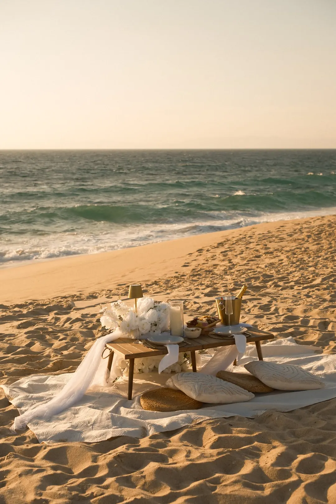A low table on linen, cushions, white flowers and Champagne on the sand