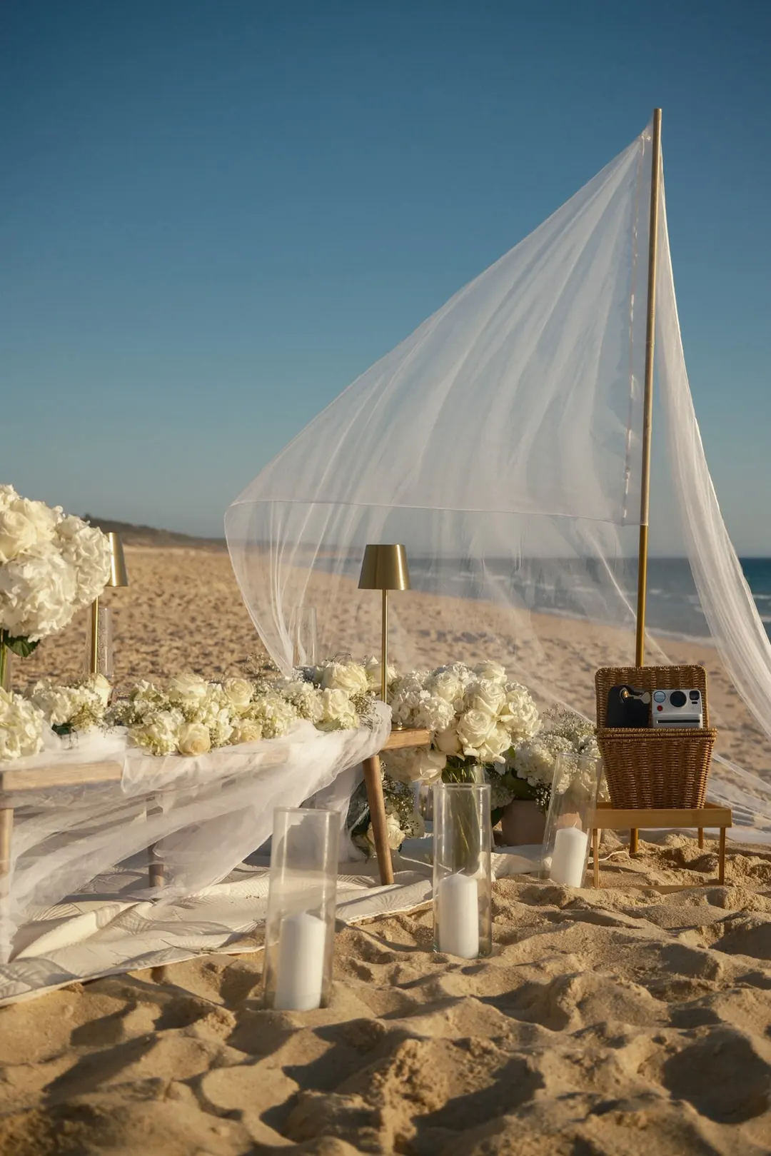 A linen sail, white hydrangeas and candles on a beach set for a proposal