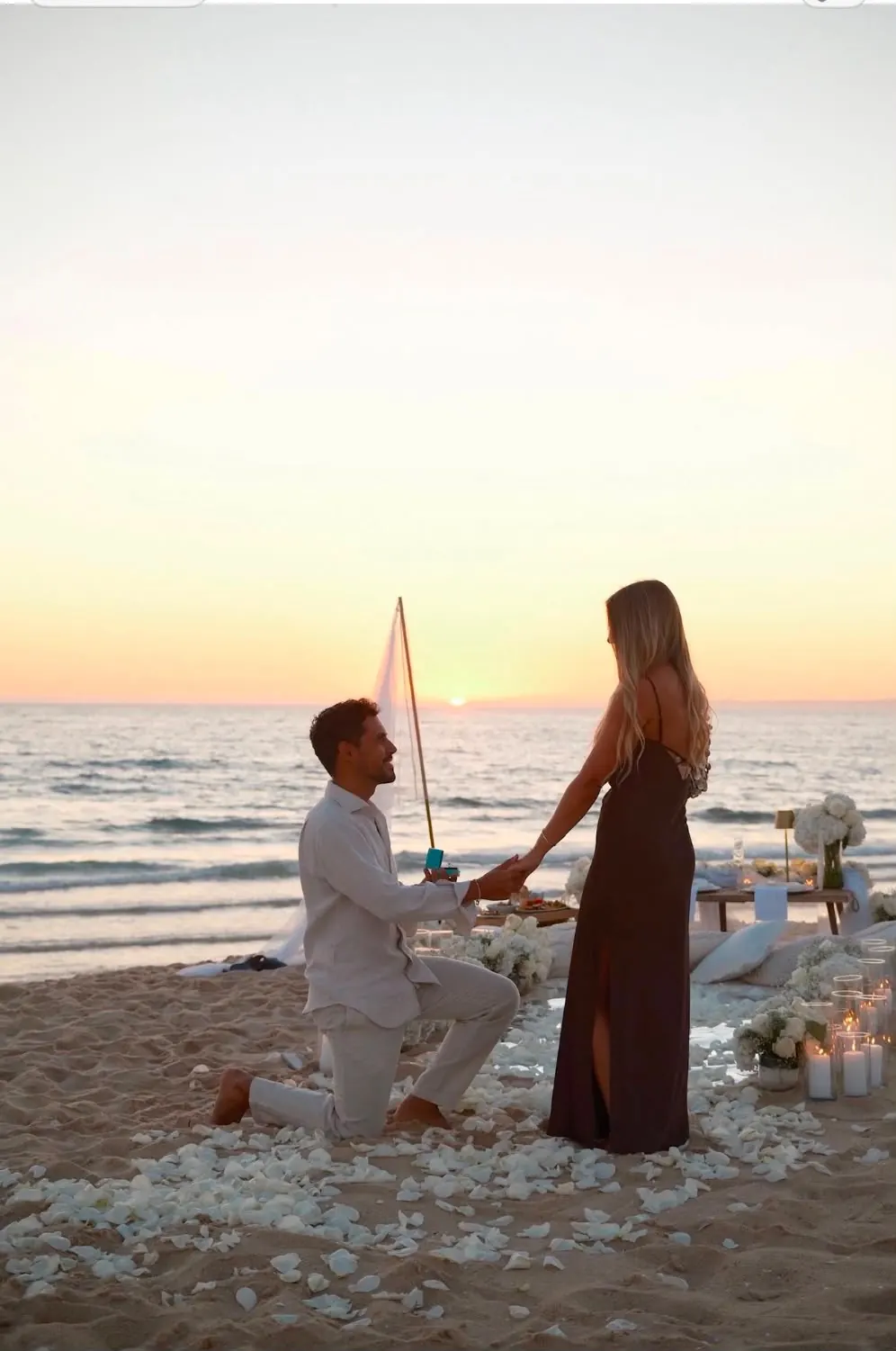 A proposal at sunset, surrounded by petals and candles