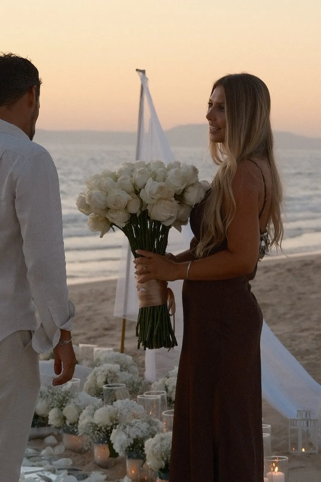She holds a bouquet of white roses after saying yes